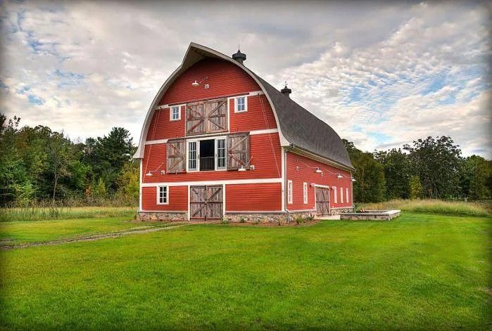 Red barn with white trim in a grassy field under a cloudy sky