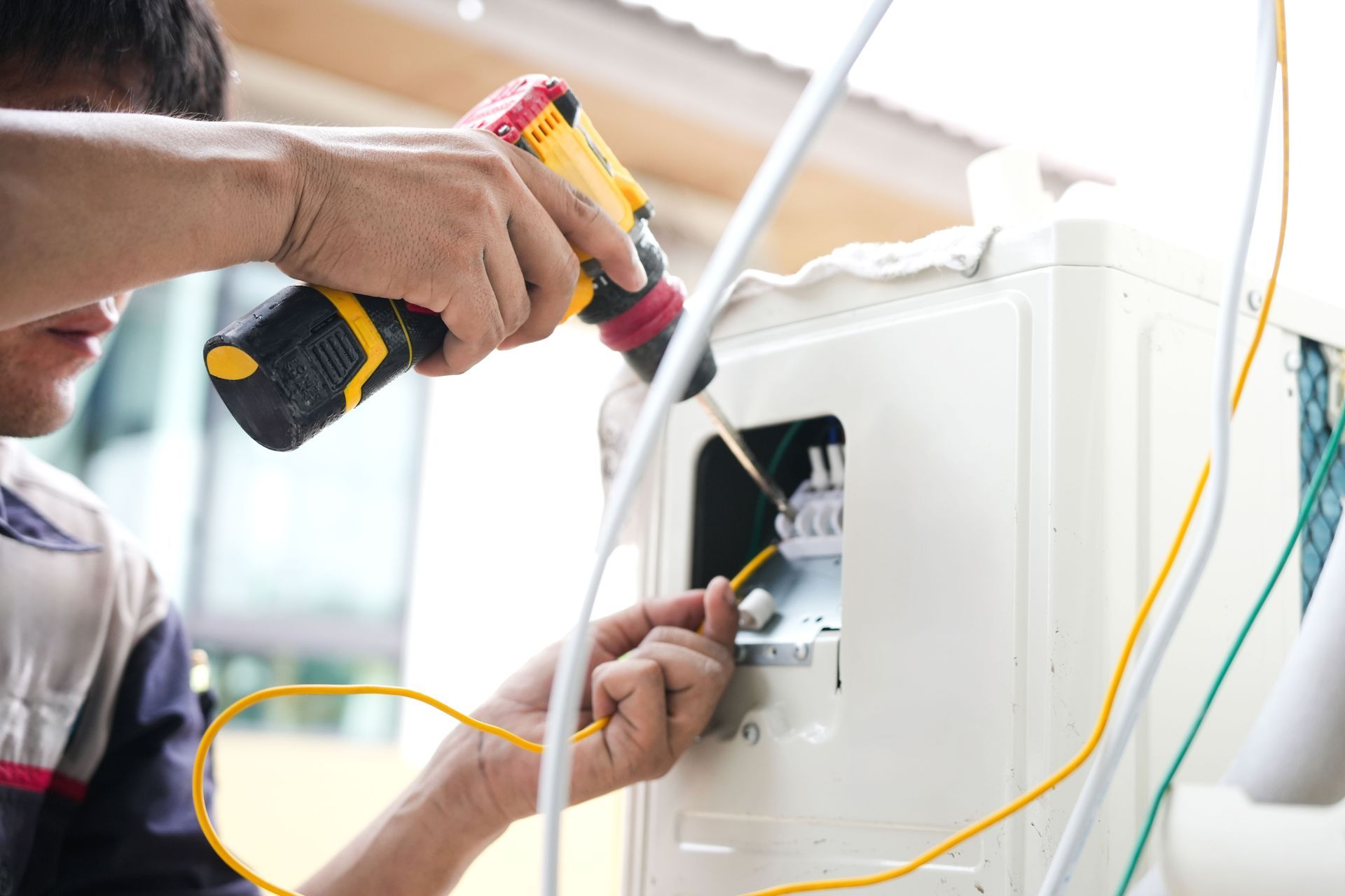Technician using a drill to repair wiring inside a white appliance cabinet