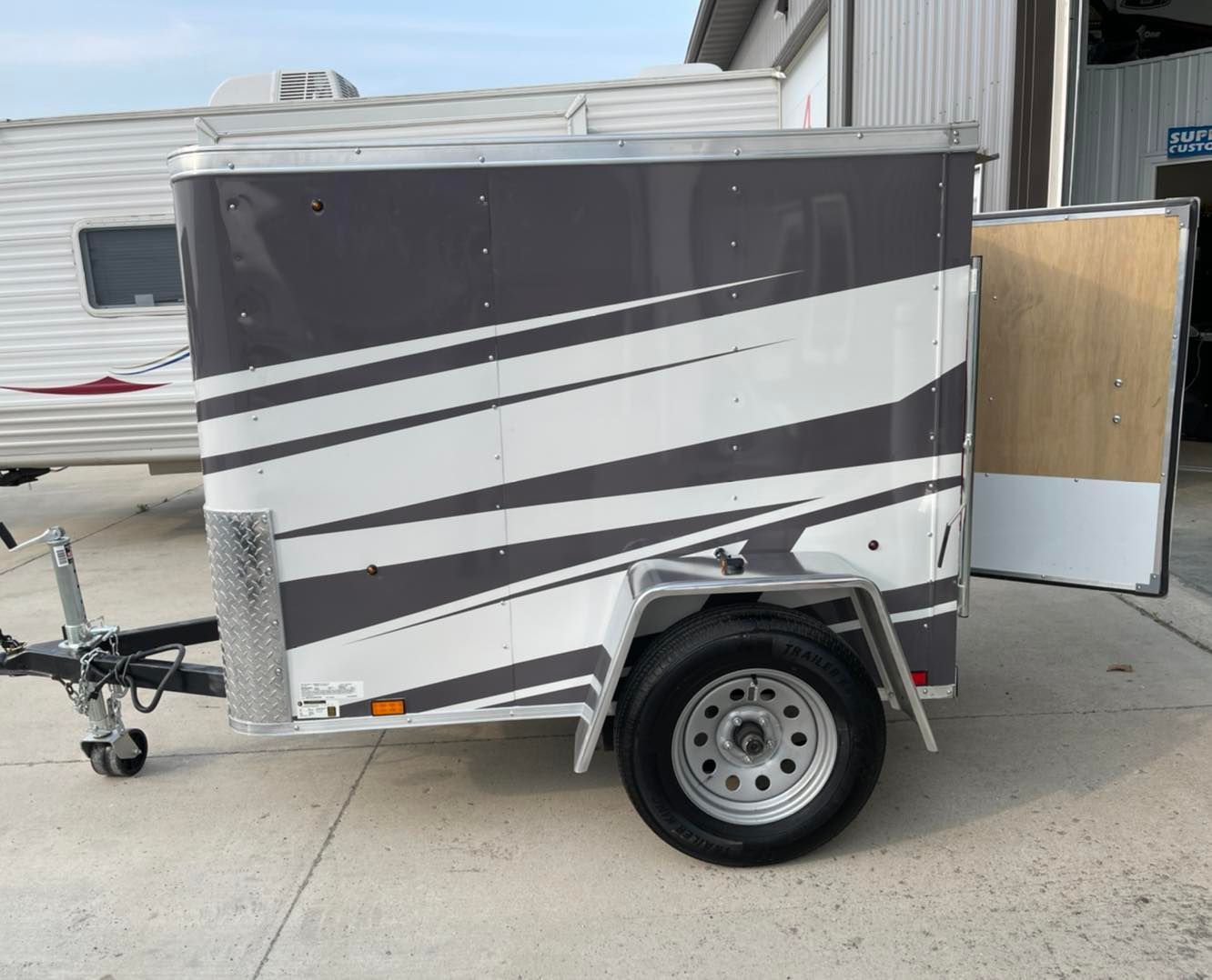 A trailer with a gray and white striped design is parked in a parking lot.