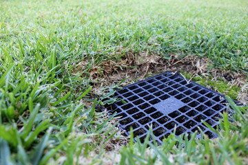 A black drain cover is sitting in the middle of a lush green lawn.
