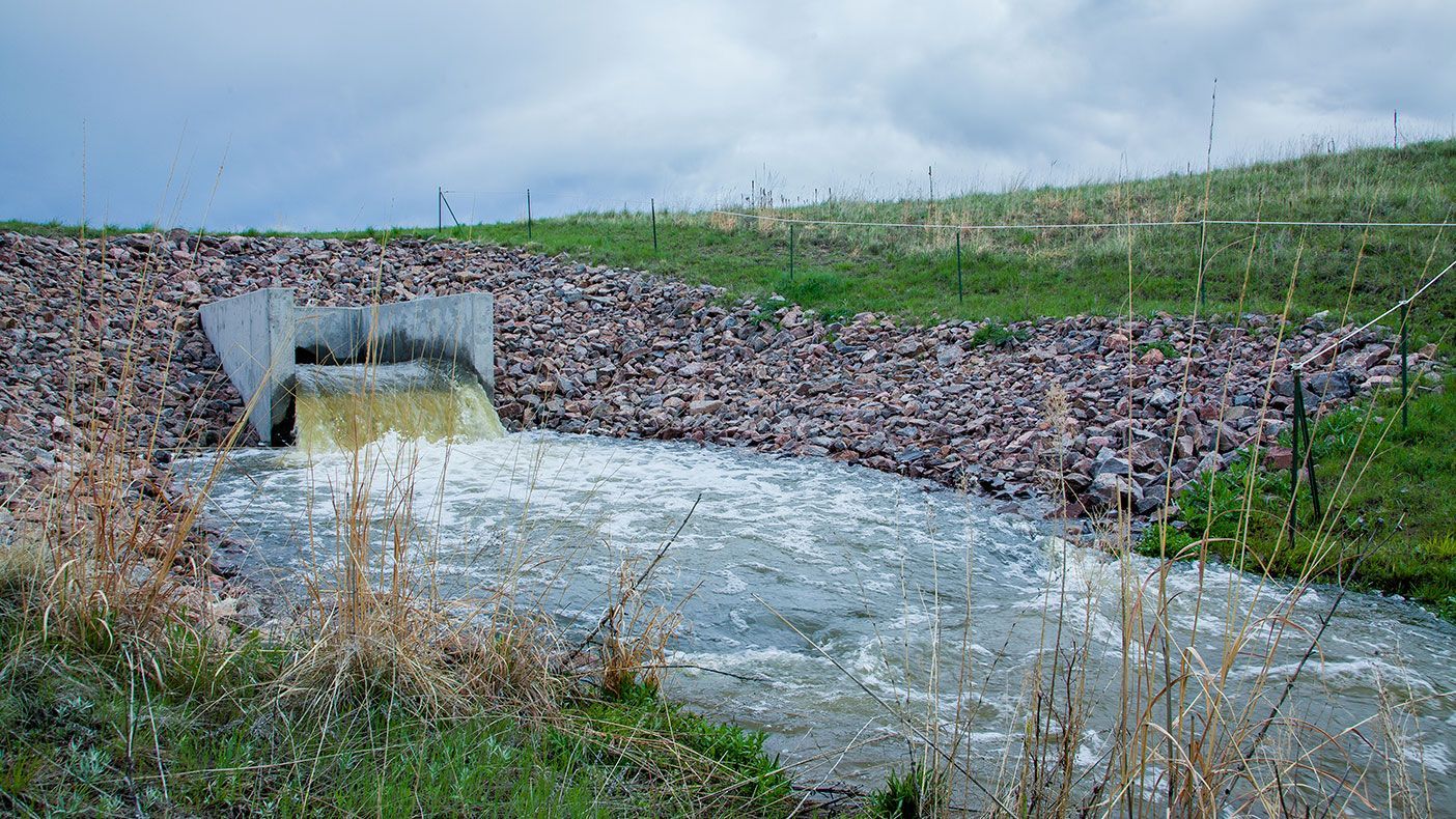 A small river flowing through a grassy field next to a rock wall.
