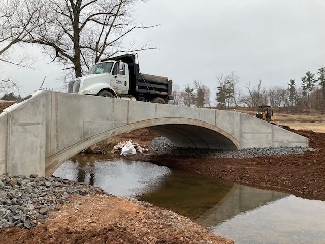 A dump truck is driving over a concrete bridge over a river.