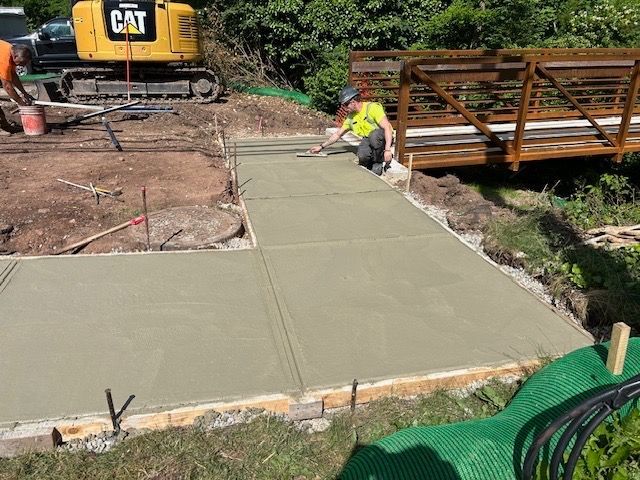 A man is working on a concrete walkway next to a cat excavator.