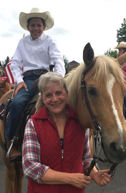 A woman is standing next to a boy on a horse.