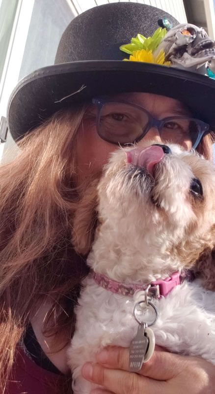 A woman in a hat is kissing a small white dog.