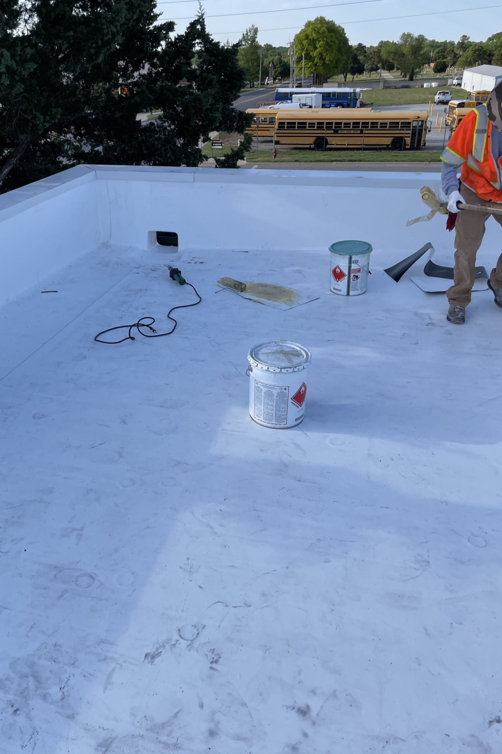 A man is standing on a white roof with buckets of paint.
