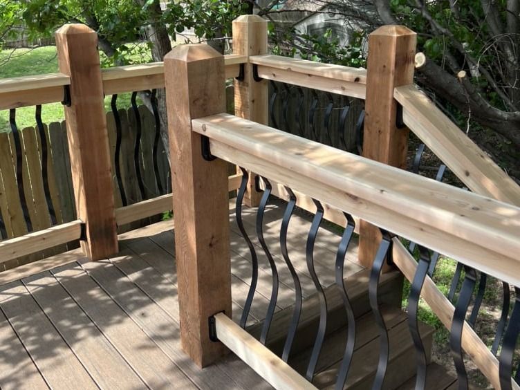 A wooden deck with a metal railing and a fence in the background.