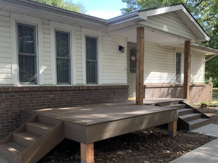 A white house with a wooden deck and stairs in front of it.