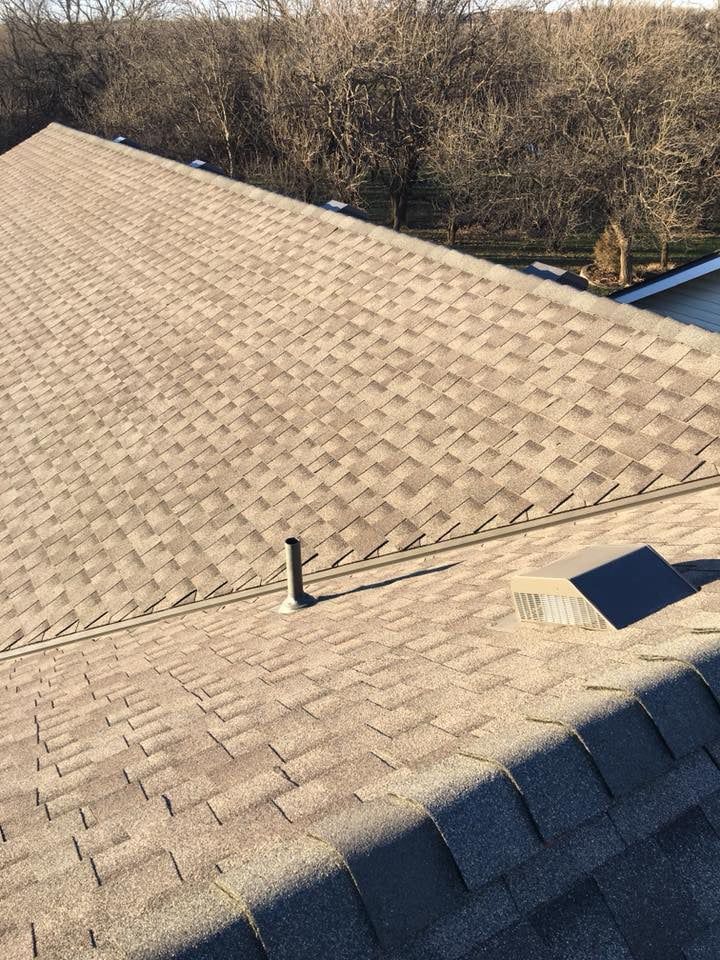 A close up of a roof with shingles on it and trees in the background.