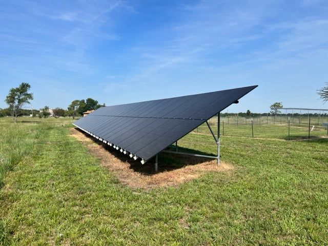 A row of solar panels sitting on top of a lush green field.