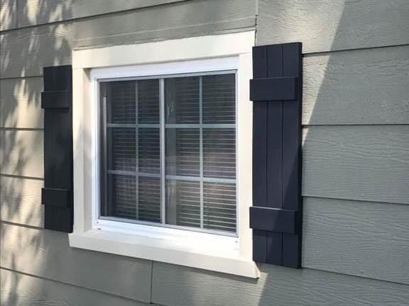 A window with black shutters on the side of a house.