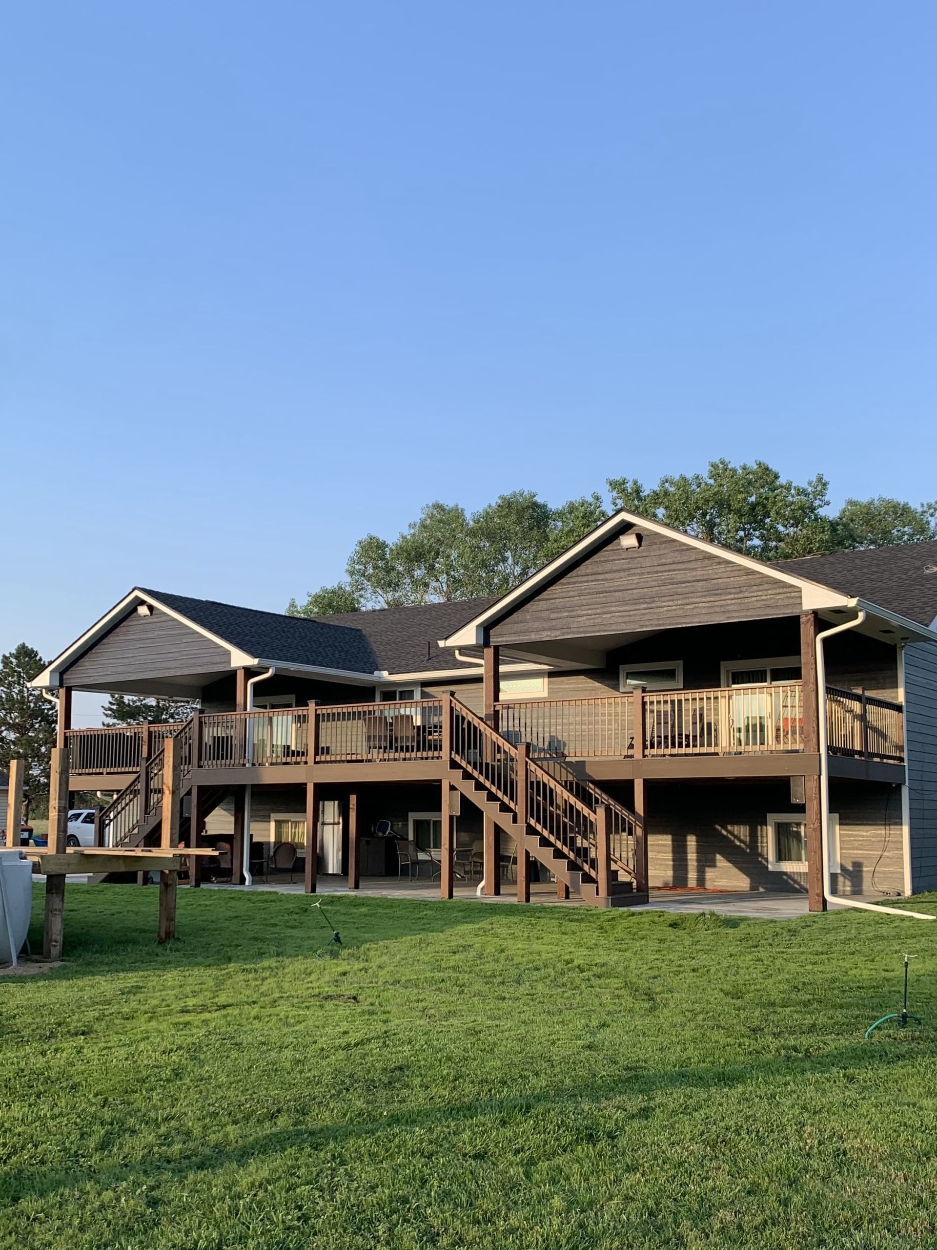 A large house with a large deck and stairs is sitting on top of a lush green field.
