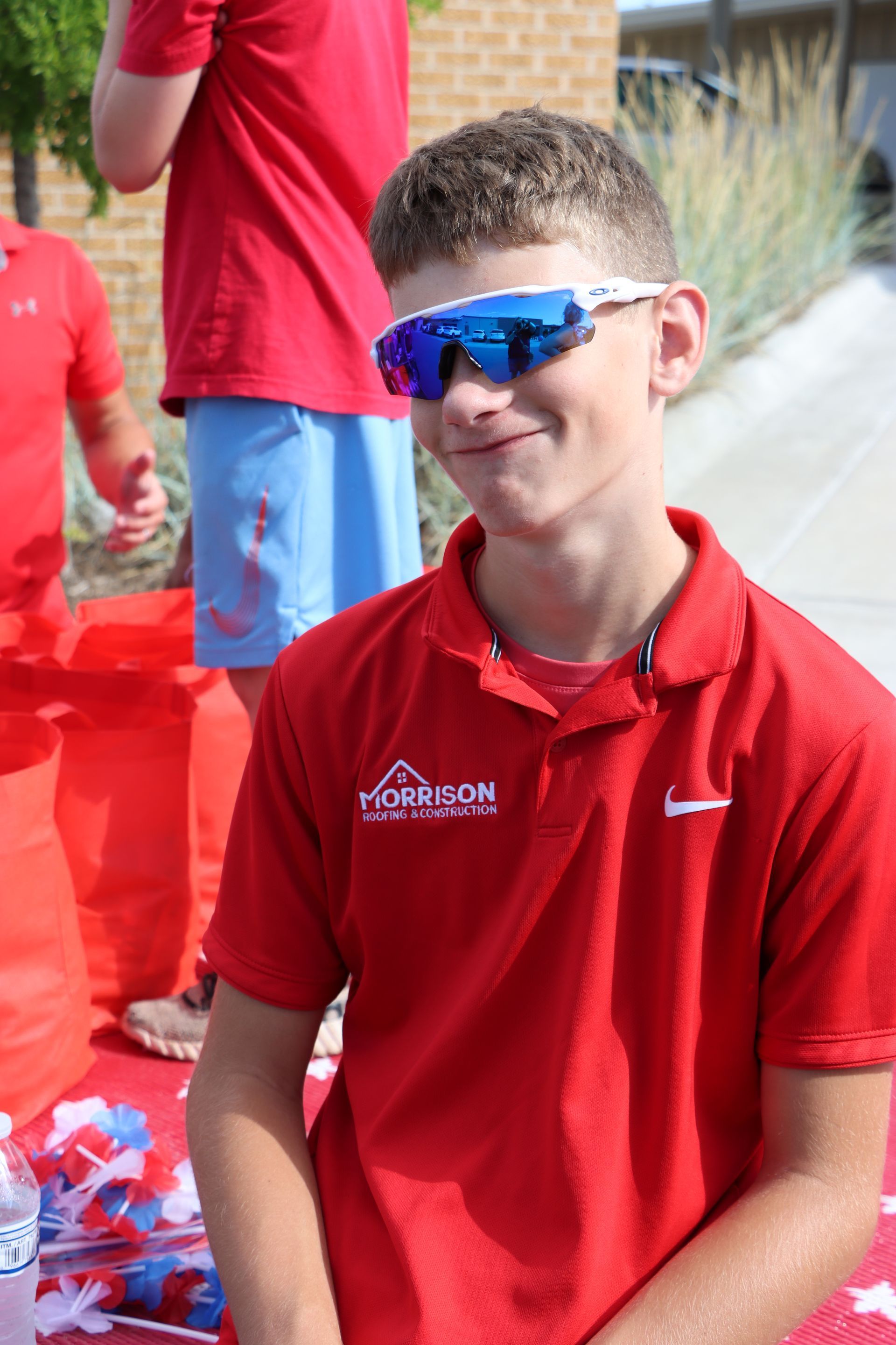A young man wearing sunglasses and a red shirt is smiling.