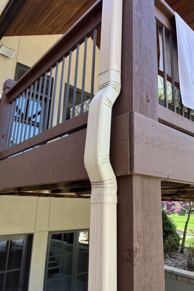 A white drainpipe is attached to the side of a wooden deck.