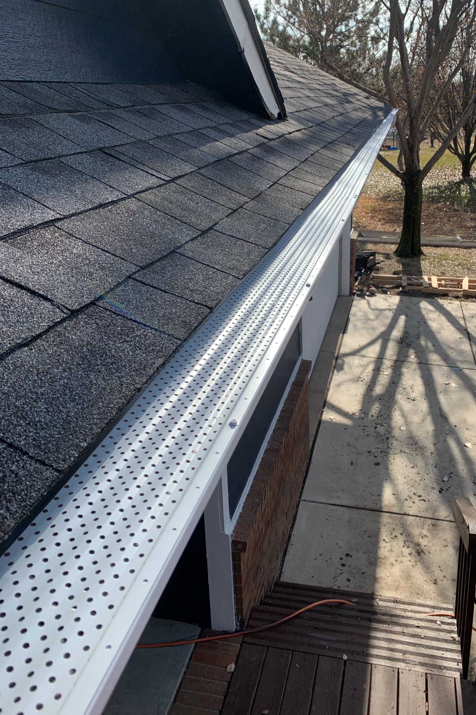 A gutter on the side of a house with a roof in the background.