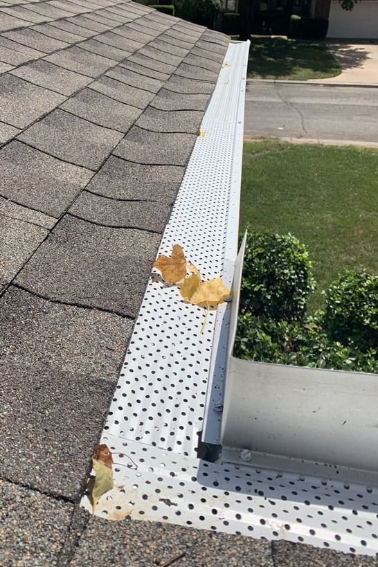 A leaf is sitting on the edge of a gutter on a roof.