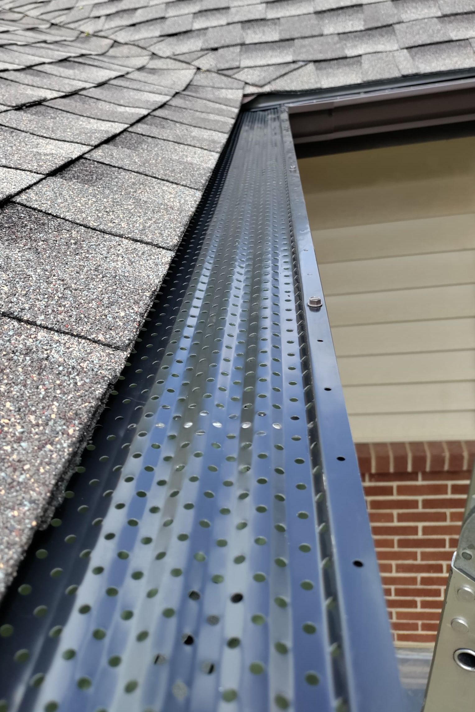 A close up of a gutter on a roof with a ladder in the background.