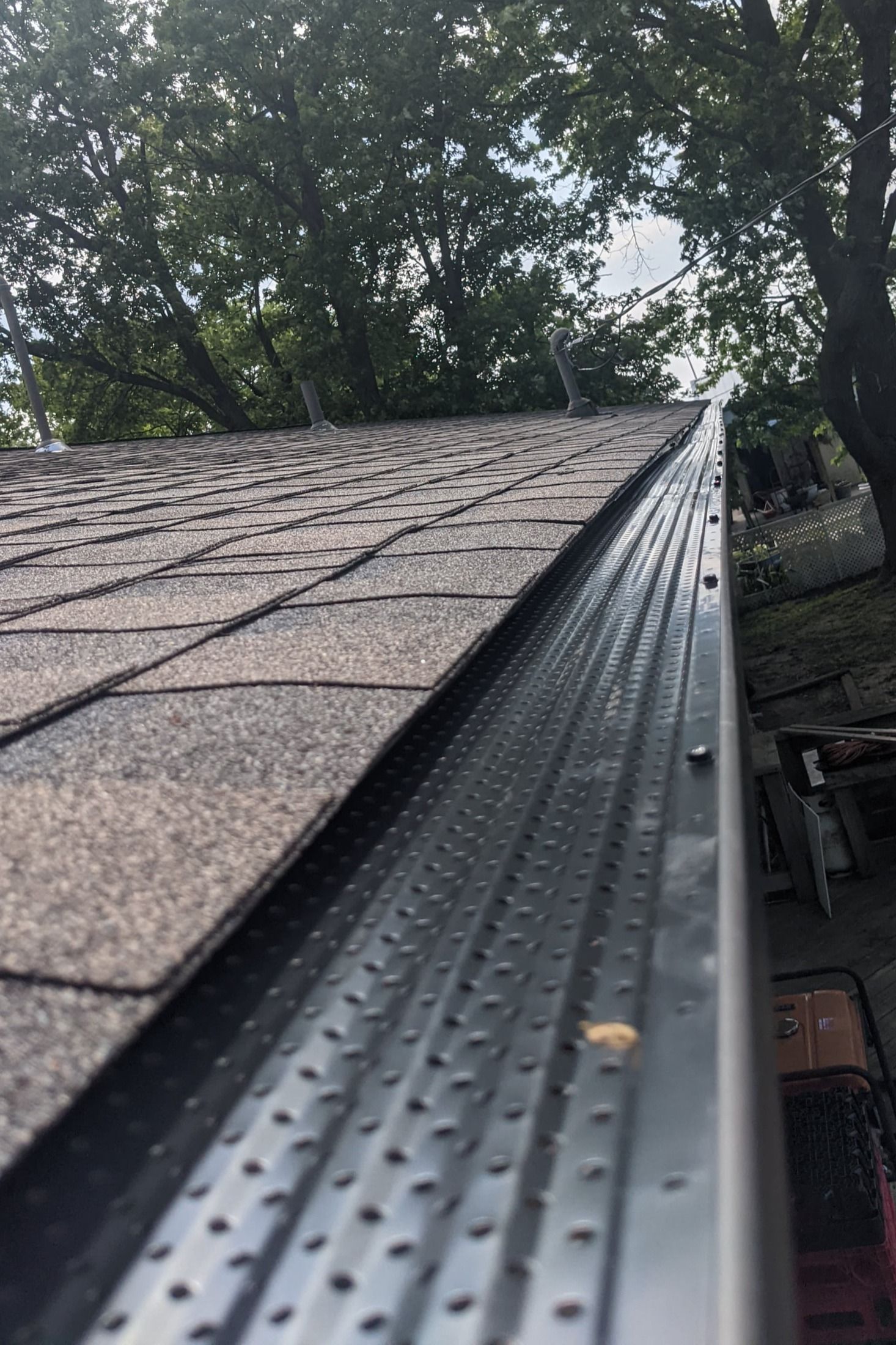 A close up of a gutter on a roof with trees in the background.