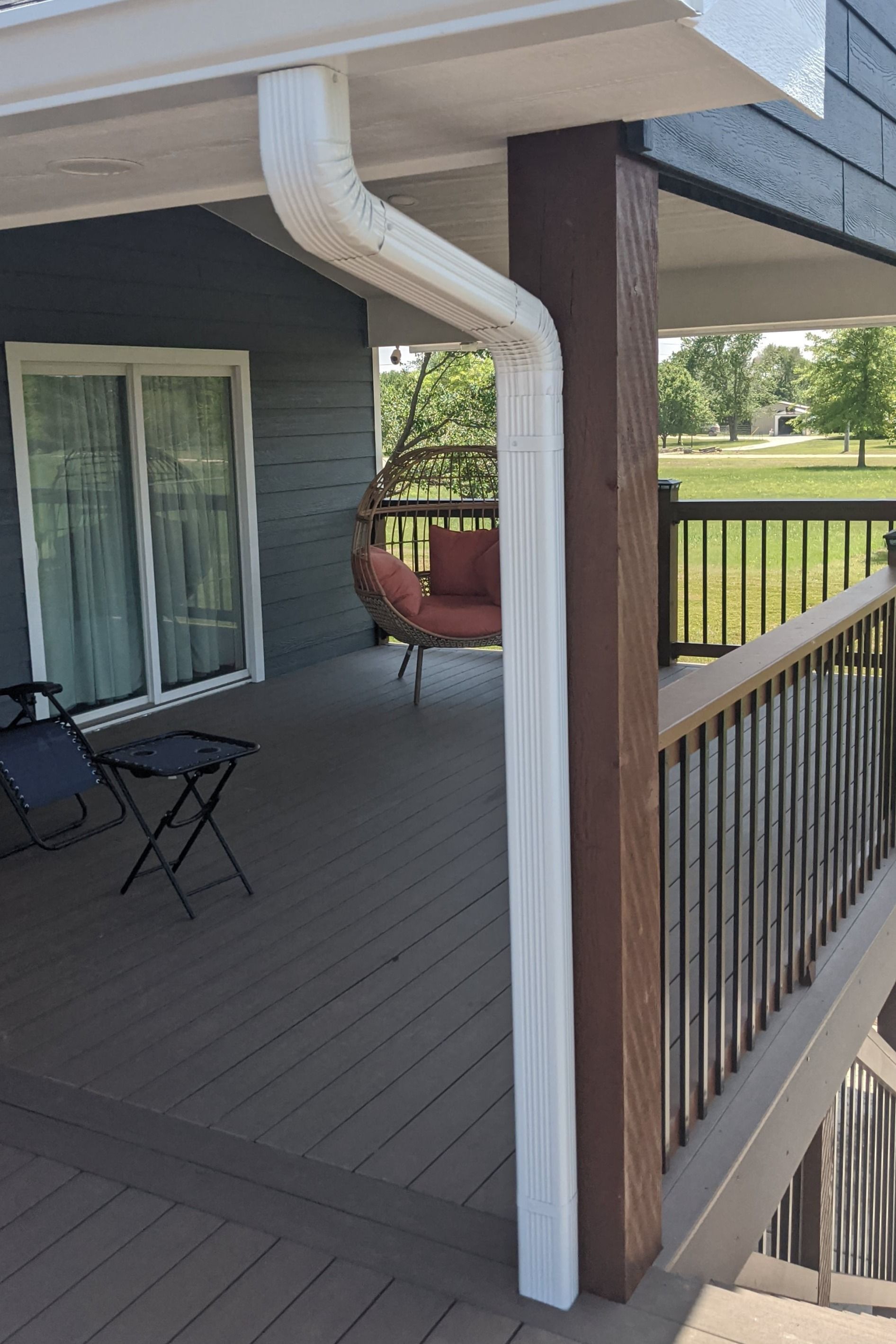 There is a porch with a white gutter and a chair on it.