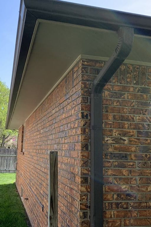 A brick house with a black gutter on the side of it.