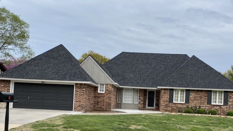 A large brick house with a black roof and a mailbox in front of it.