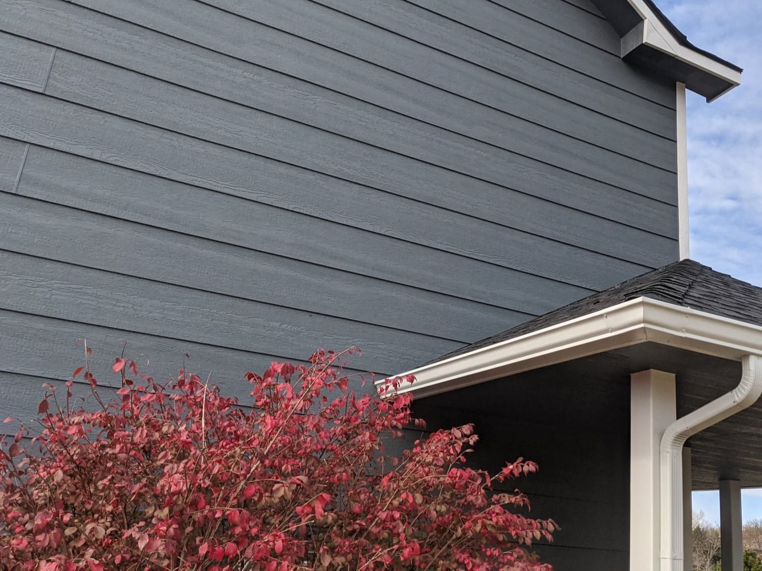 The side of a house with a tree in front of it.