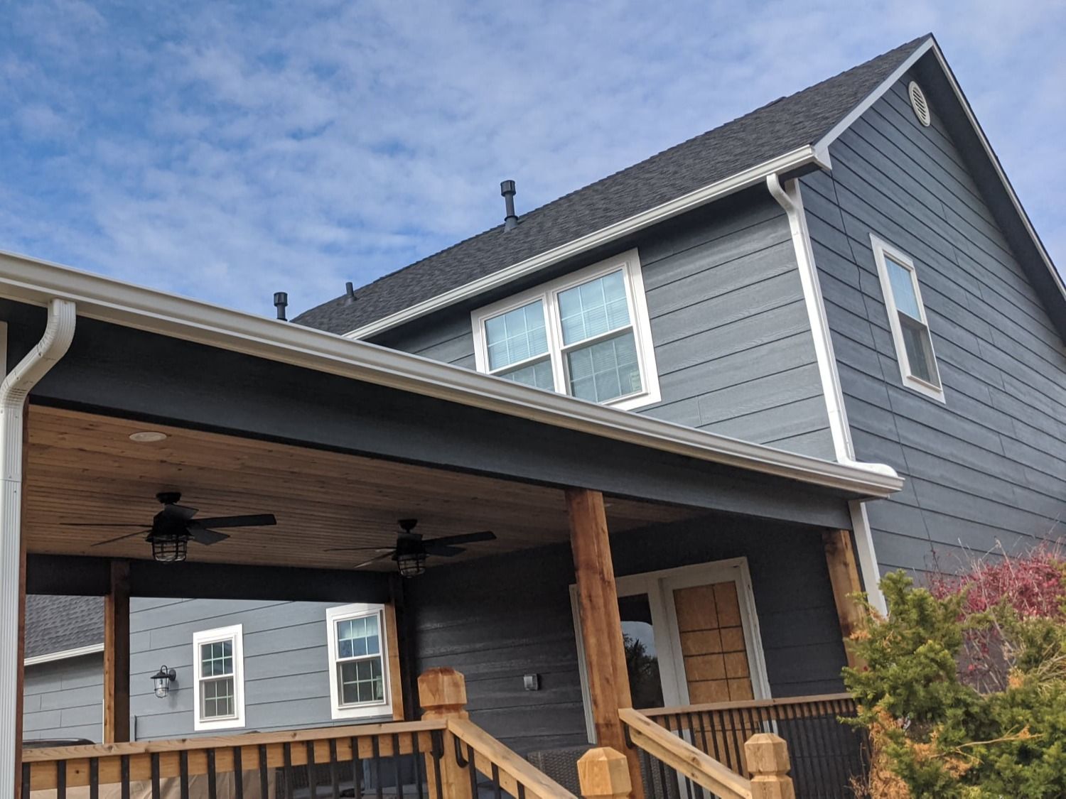 A large gray house with a porch and a ceiling fan.