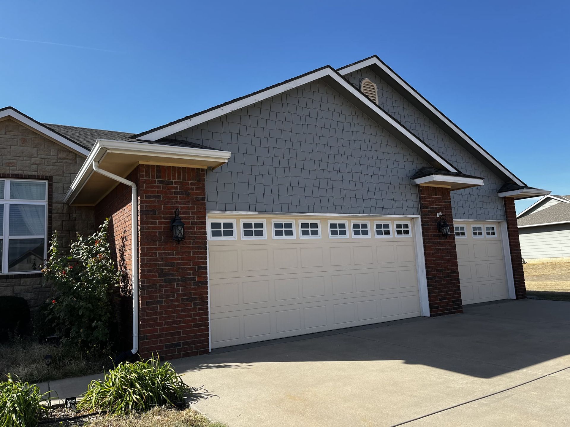 A brick house with two white garage doors and a blue sky in the background
