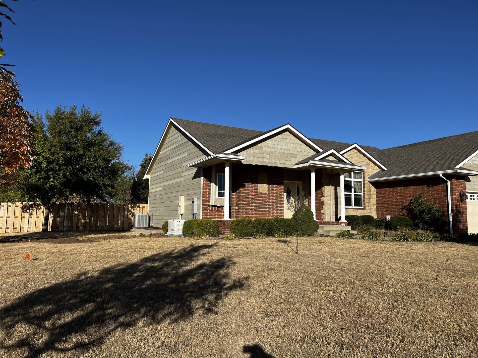 A brick house with a gray siding and a gray roof is sitting on top of a gravel lot.