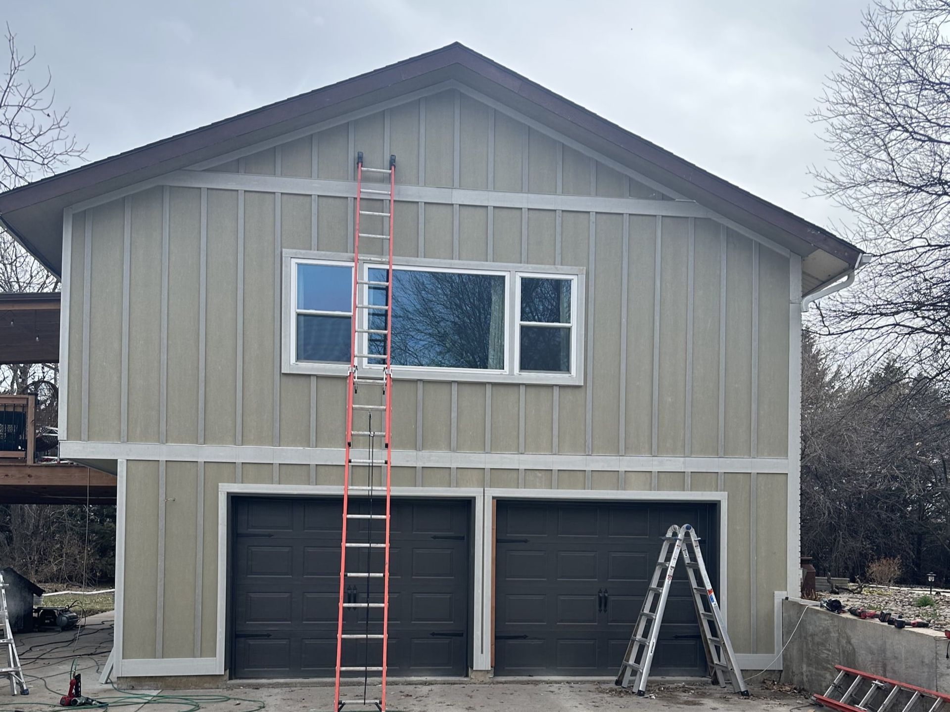 A large house with two garage doors and a ladder in front of it.