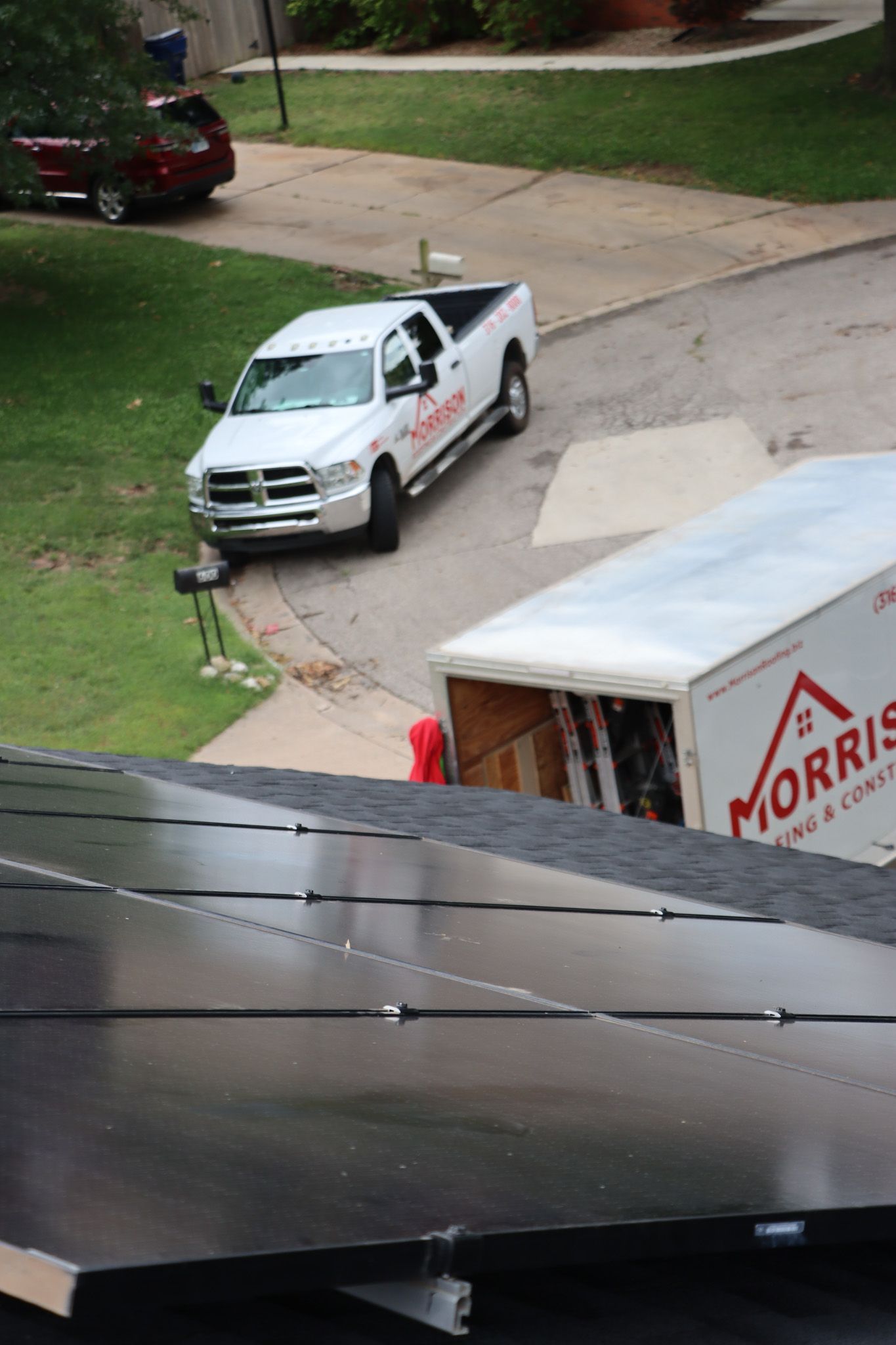 A white truck is parked next to a white Morris Roofing truck.