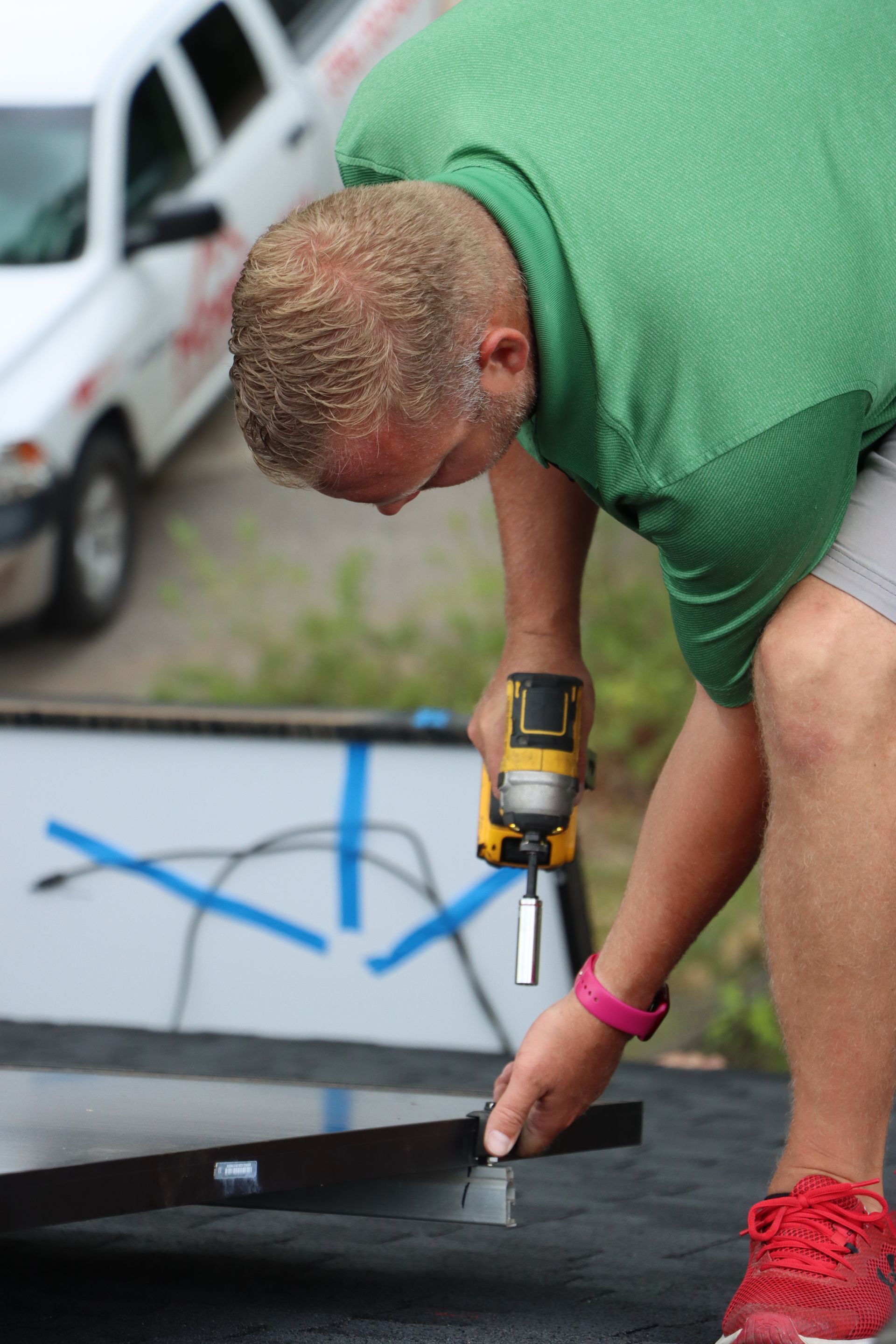 A man in a green shirt is using a drill on a piece of metal.
