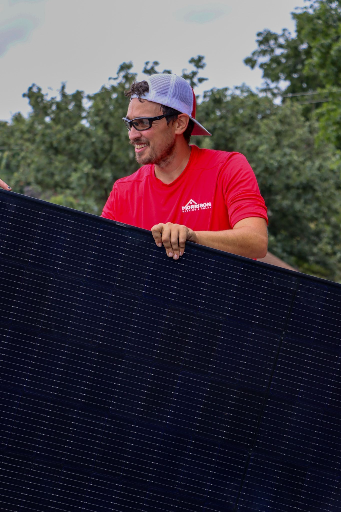 A man in a red shirt and purple hat is holding a black blanket.