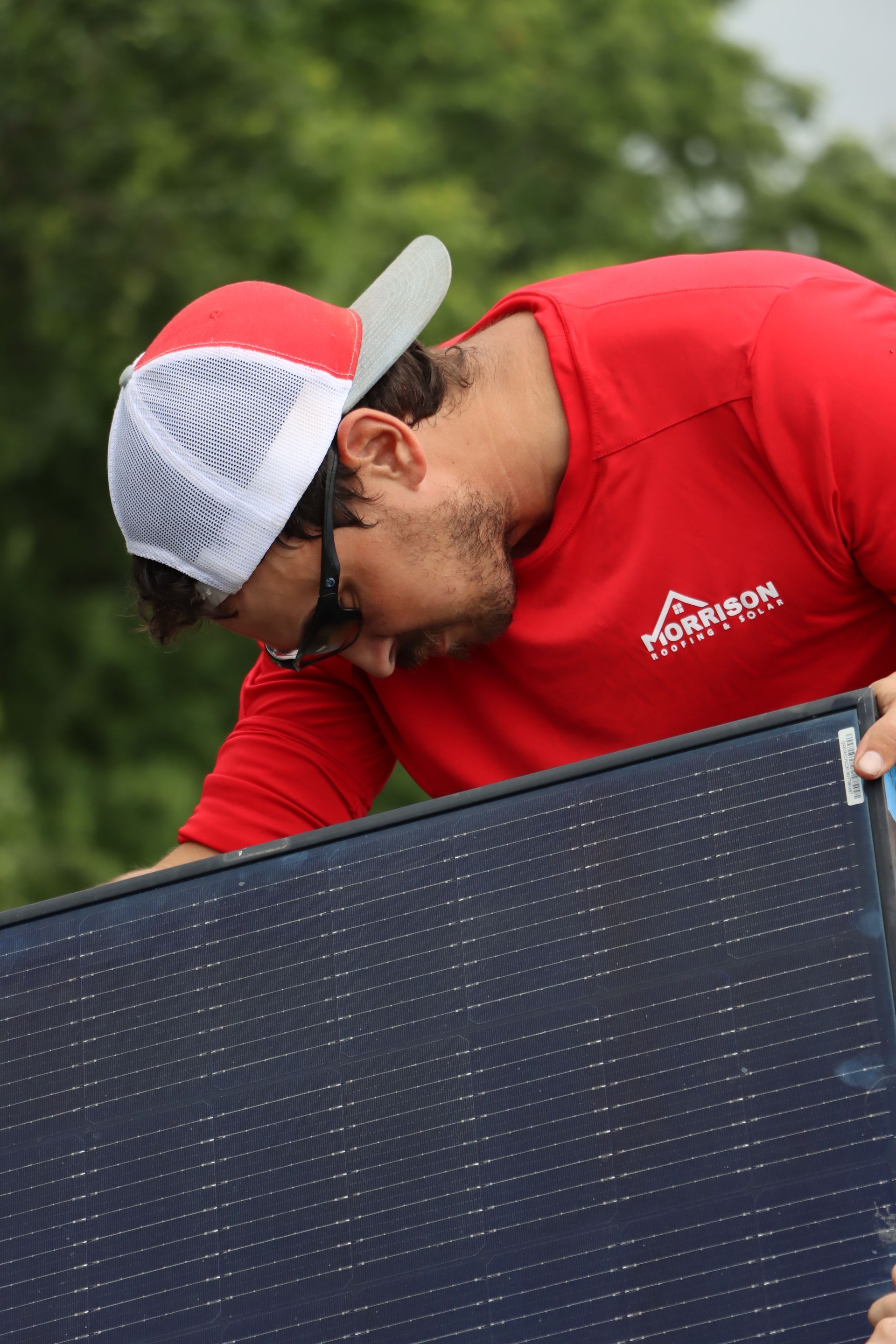 A man wearing a red shirt and a white hat is working on a solar panel.