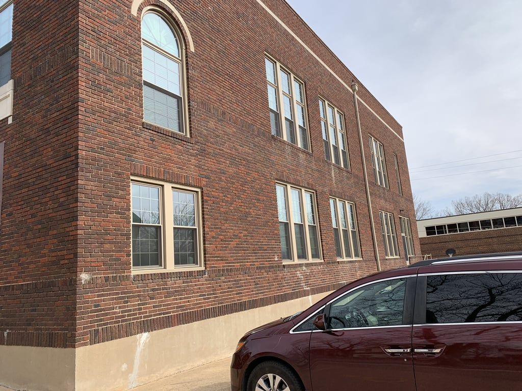 A red minivan is parked in front of a large brick building.