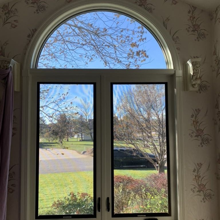 A window with a curved arch and a view of a field and trees.