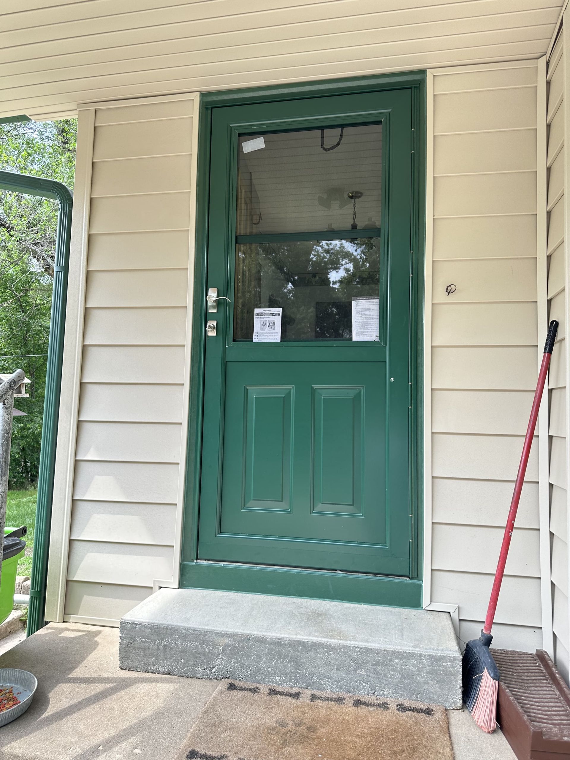 A green door with a glass window is on a white house.