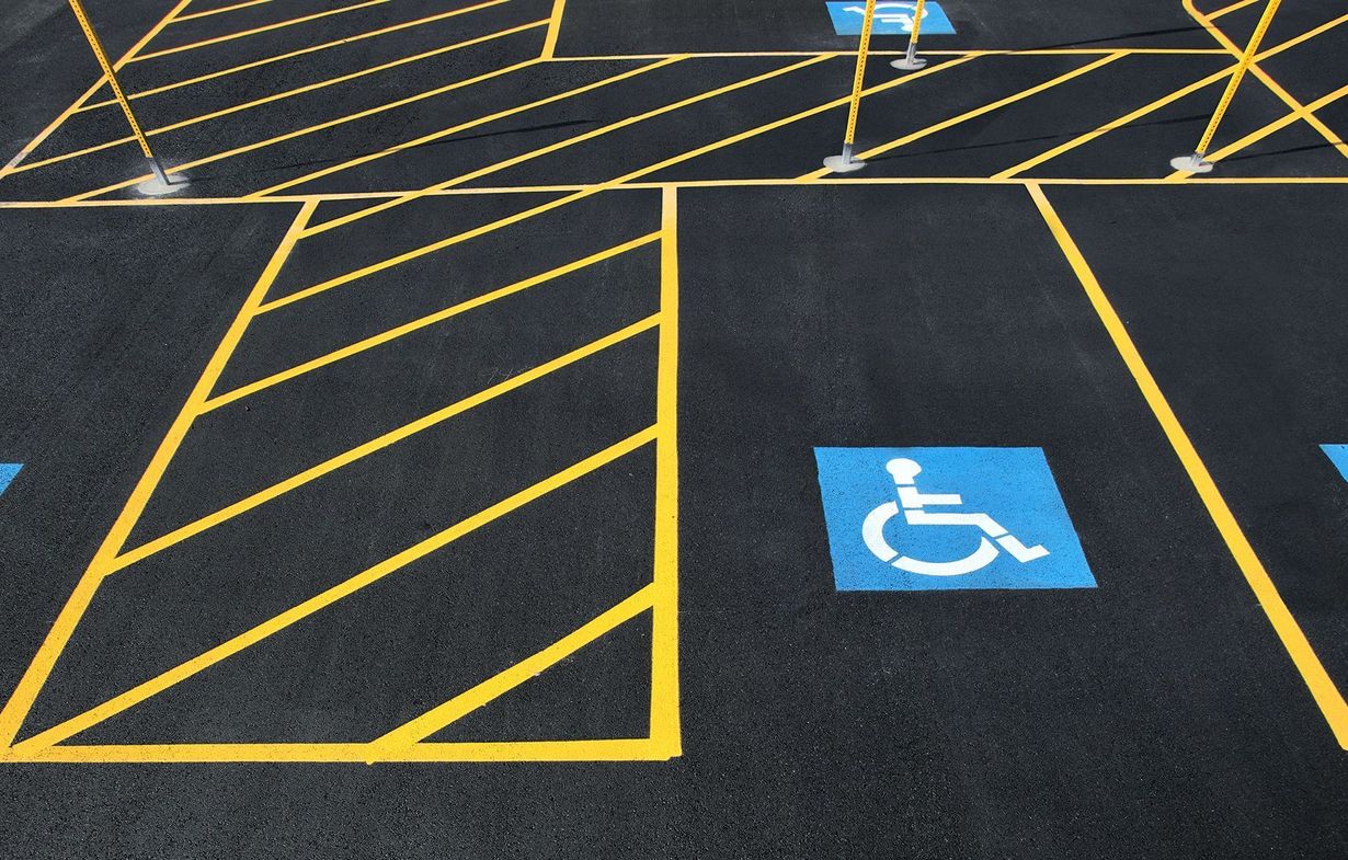 Blue handicap parking symbol on asphalt next to yellow striped no-parking markings.