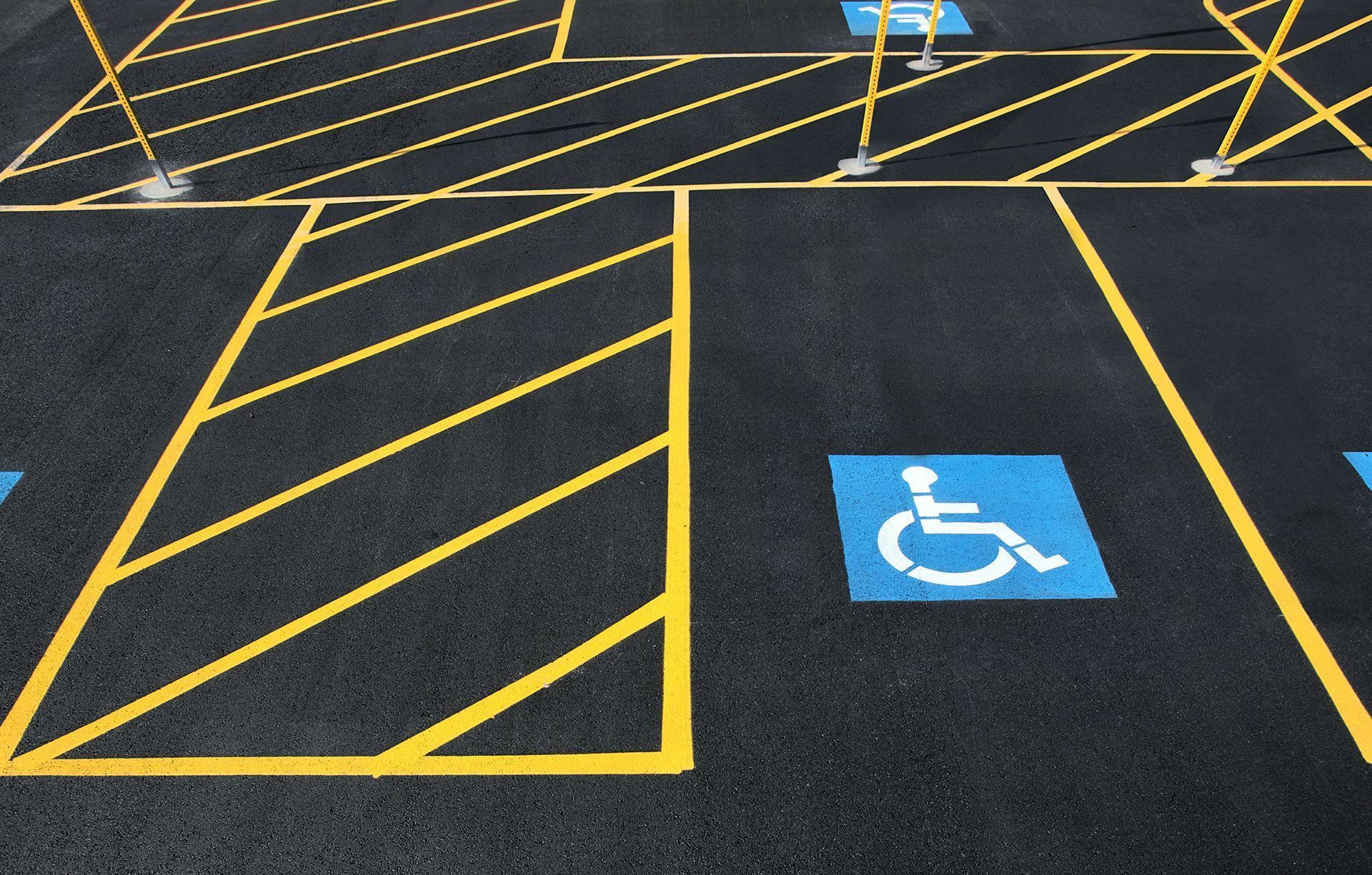 Blue handicap parking symbol on asphalt next to yellow striped no-parking markings.