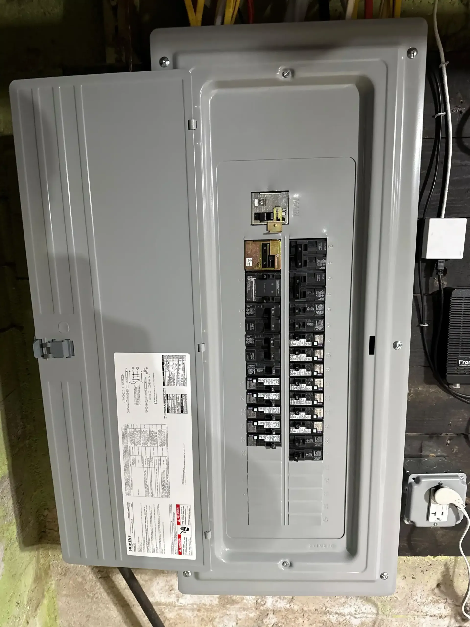 Gray electrical panel with open cover, revealing circuit breakers.