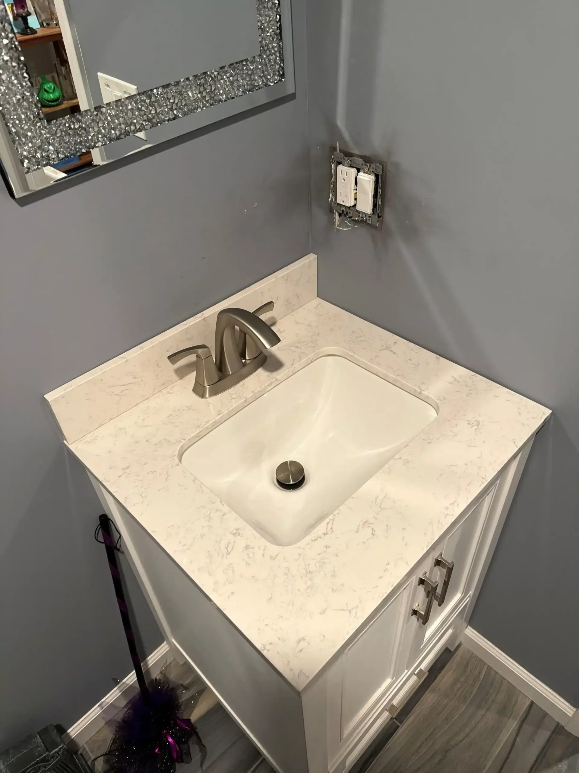 Small white vanity with a sink in a bathroom, with a gray wall and a sparkly mirror.