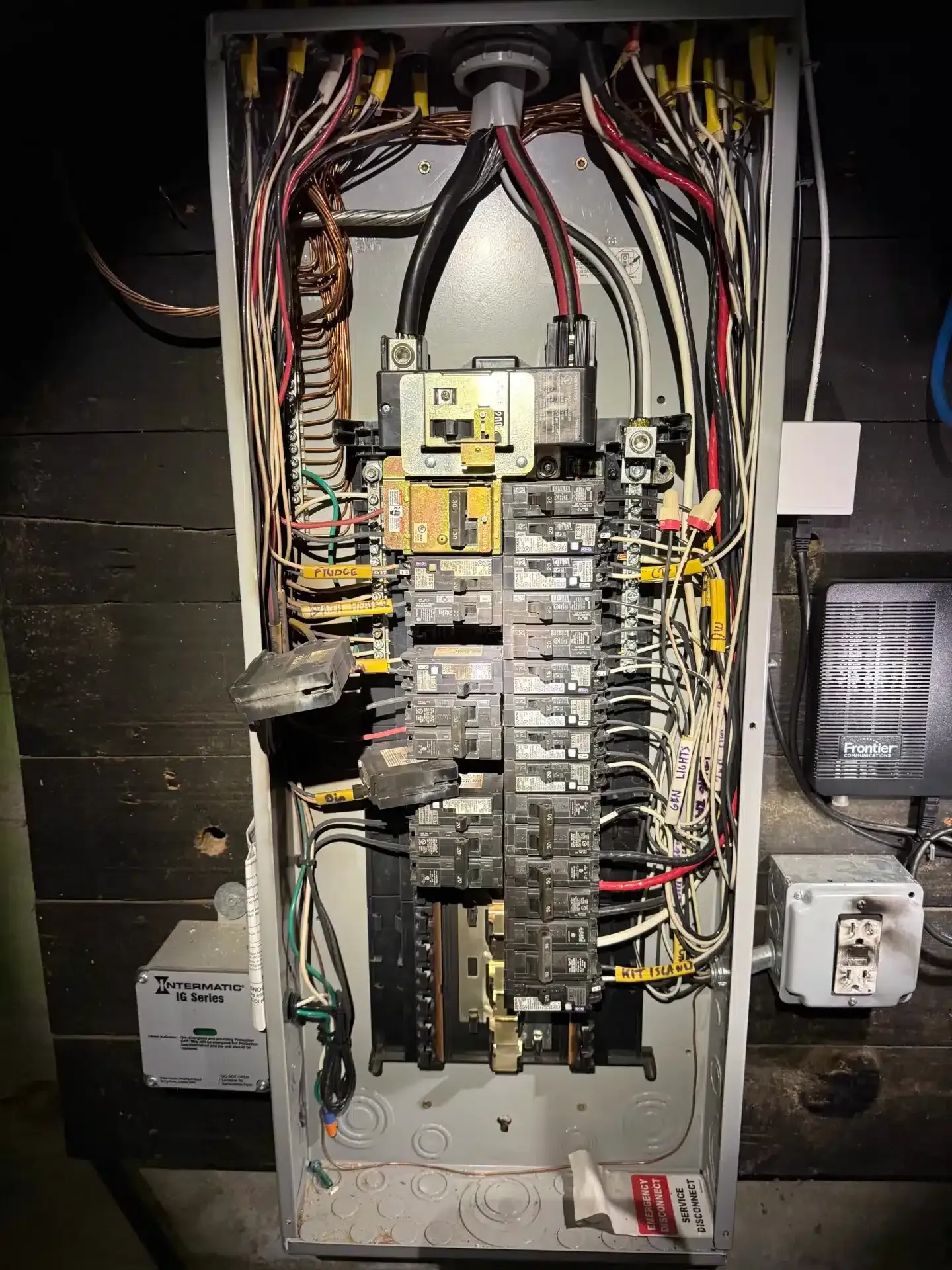Electrical panel with numerous wires and circuit breakers, housed in a metal box.