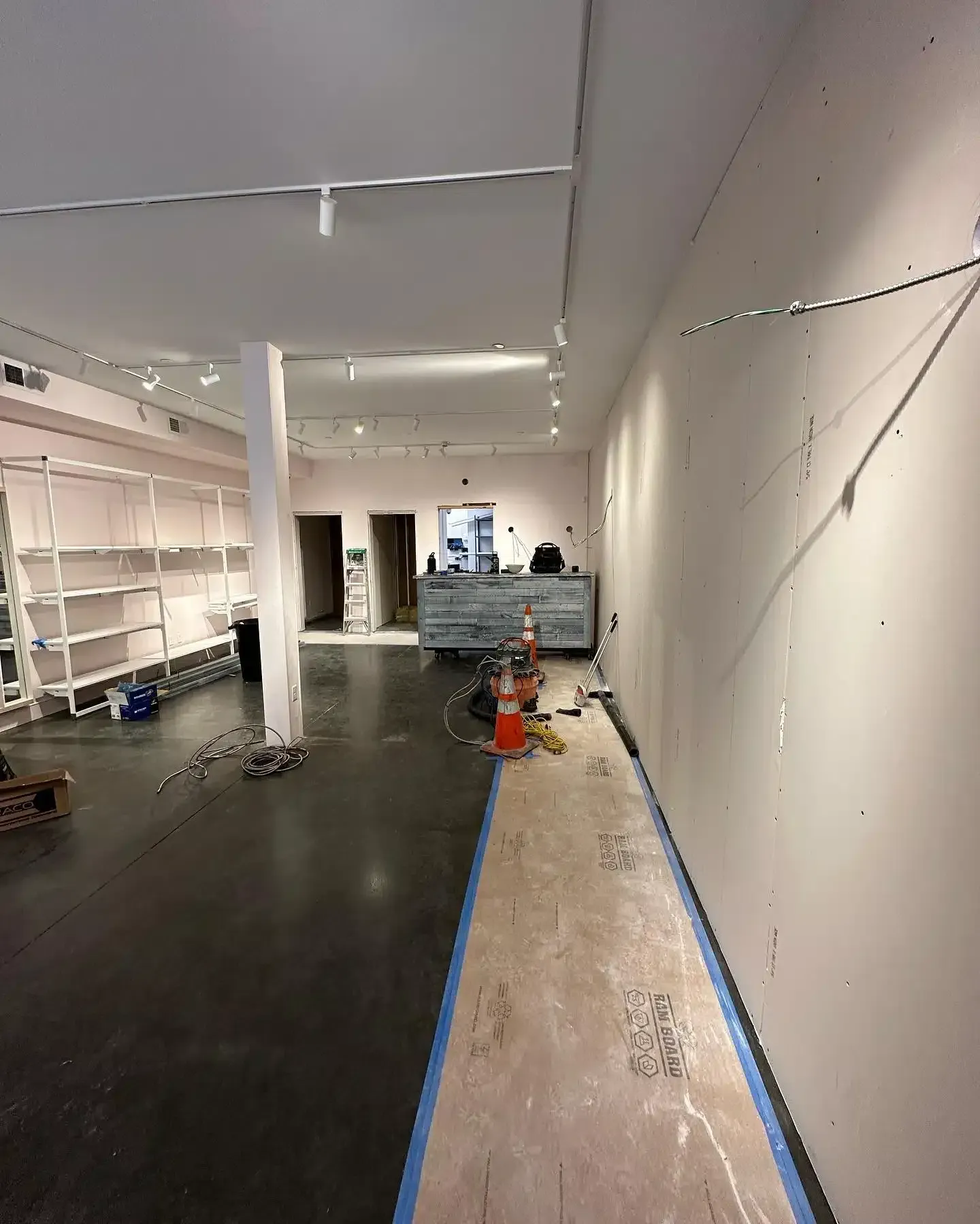Interior of a store under construction with dark floor and light walls. Shelving and a desk are visible.