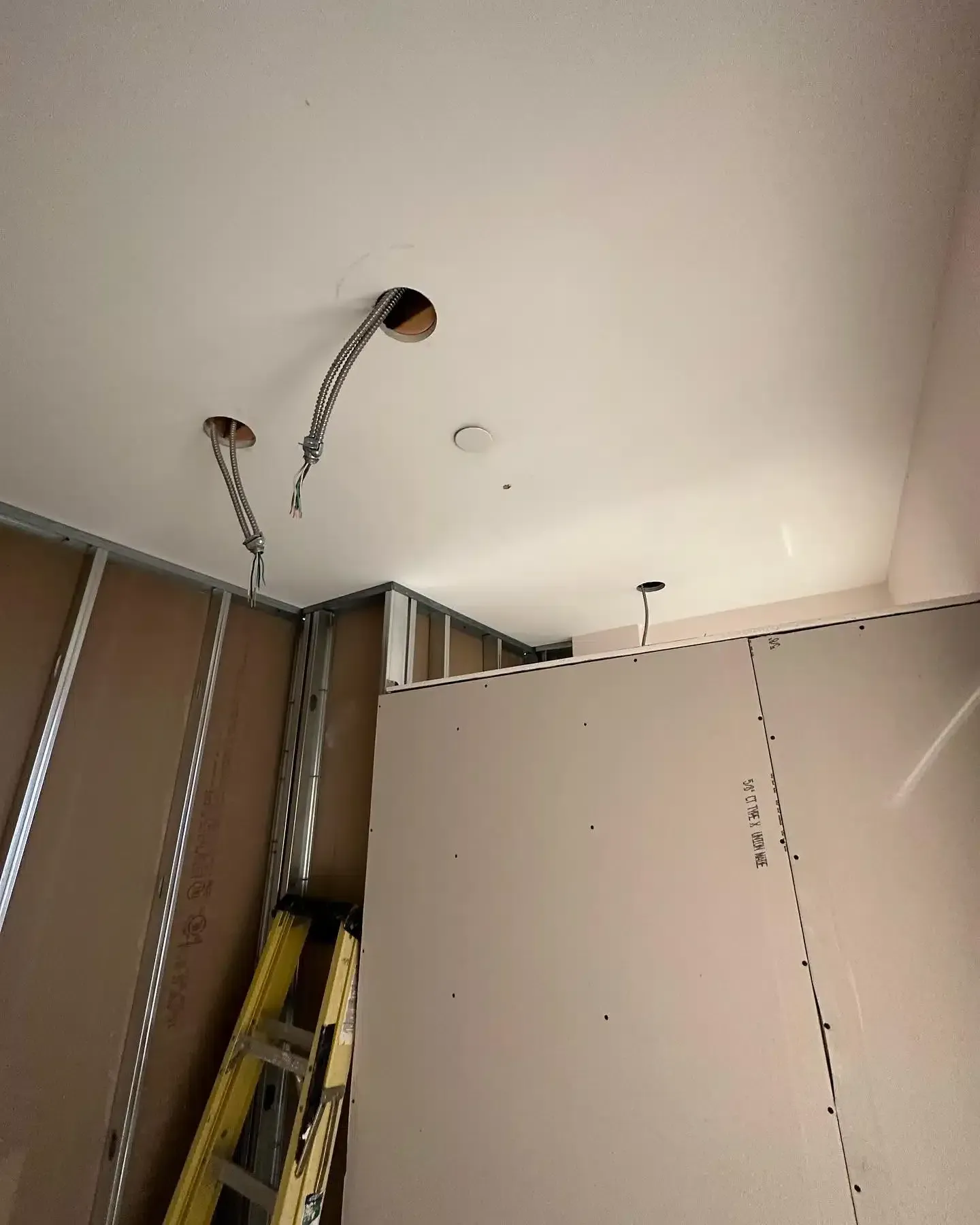 Ceiling with exposed wiring, drywall, metal studs, and ladder; interior construction in progress.