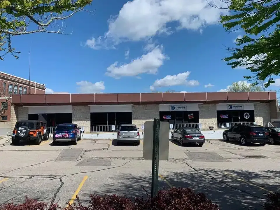 Building with parking spots. Brown and white facade, cars parked outside. Blue sky with clouds.