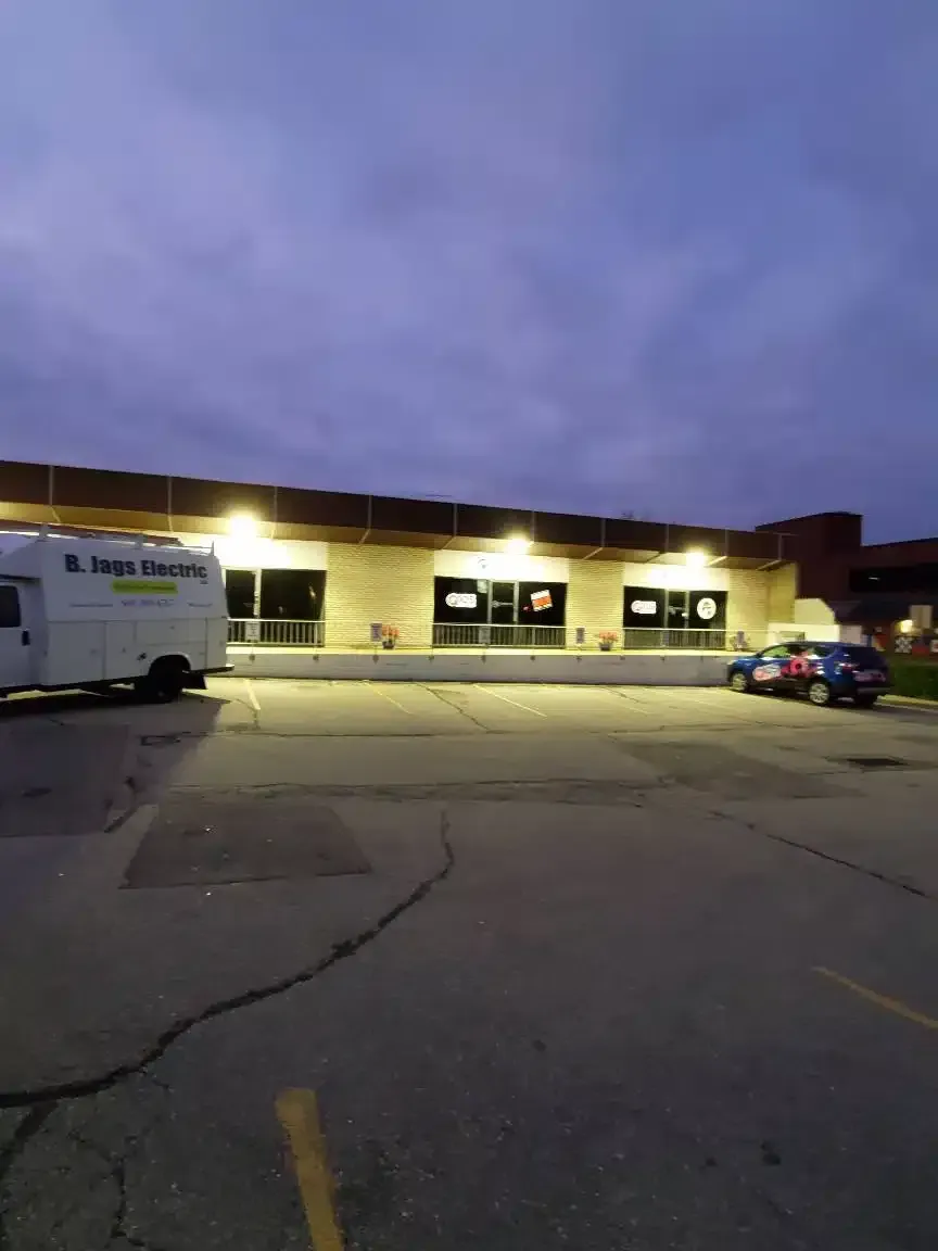 Exterior view of a commercial building at dusk; lit windows, a truck, car parked in a parking lot.
