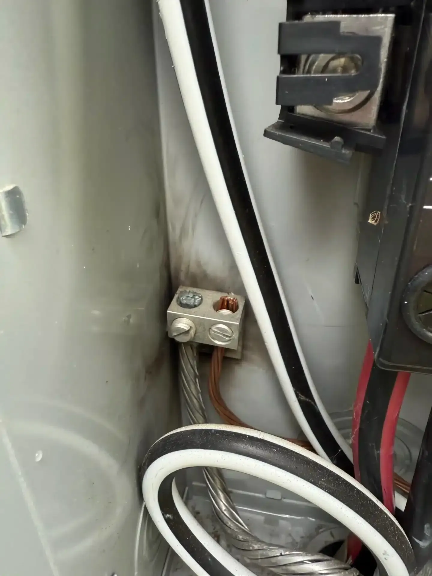 Electrical panel with a ground wire connected to a terminal, showing evidence of arcing or burning.