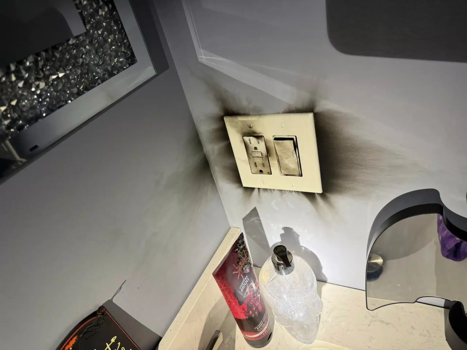 Burnt electrical outlet and light switch on a gray wall, smoke damage.