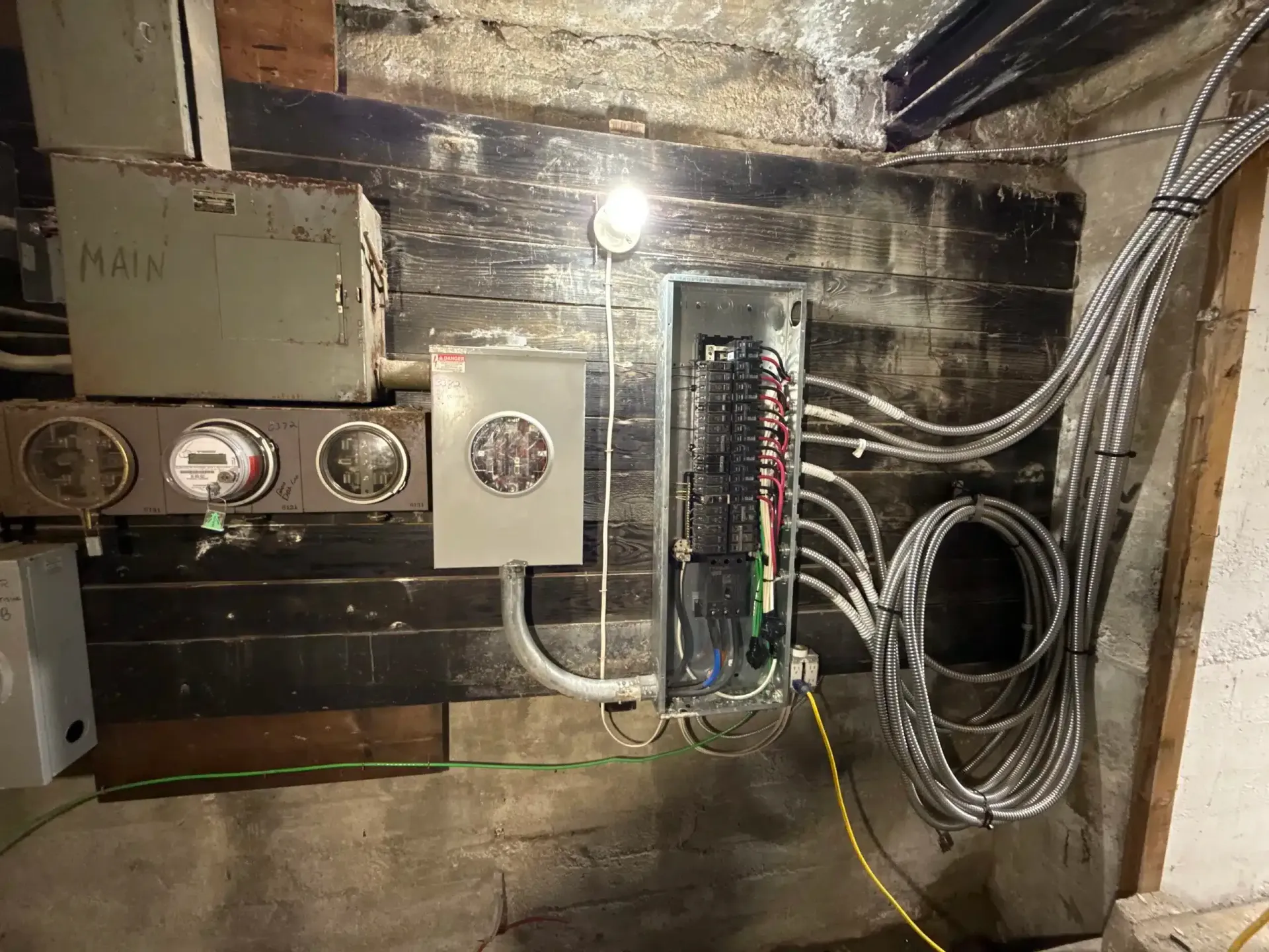 Electrical panel with meters and wiring on a dark, rough wall.