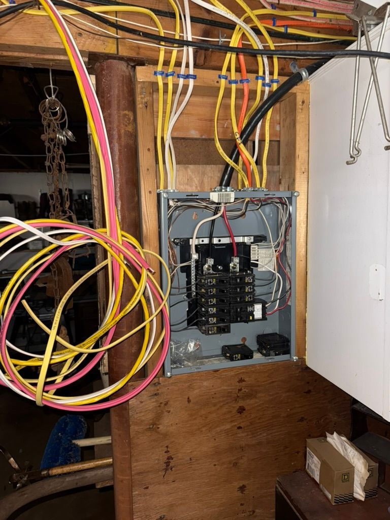 Electrical panel with numerous wires, mounted on a wood wall. Wires are yellow, pink, and white.